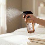 Hand spraying LEAFI Aroma Champagne Toast room spray mist over fresh white bed linen in a bright bedroom