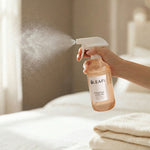 Hand spraying LEAFI Aroma Freesia & Pear room spray mist over fresh bed linen in a bright bedroom