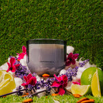 LEAFI Allure Cotton Blossom & Lily candle (400g) surrounded by floral and citrus elements on a grass background.