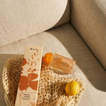 LEAFI Shadows Freesia & Pear home diffuser (200ml) packaging with a net bag on a beige sofa.