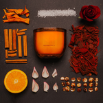 LEAFI Allure Orange & Sandalwood candle (400g) surrounded by cinnamon sticks, orange slices, rose petals, and other elements on a dark surface.